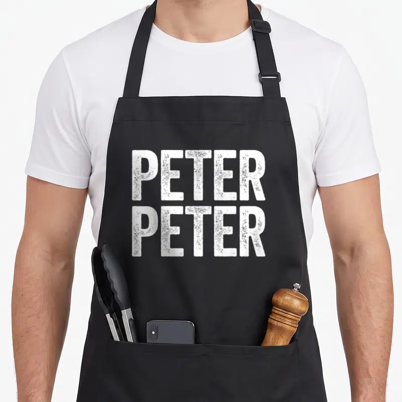 Eater pumpkin apron - White stacked text reading PETER PETER in a distressed font style — shown on a black cotton canvas apron against a white background