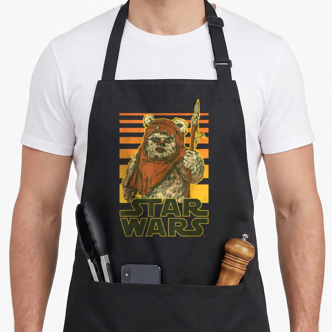 Wicket sunset apron - Ewok holding spear, STAR WARS text, orange yellow stripes, distressed print — shown on a black cotton canvas apron against a white background