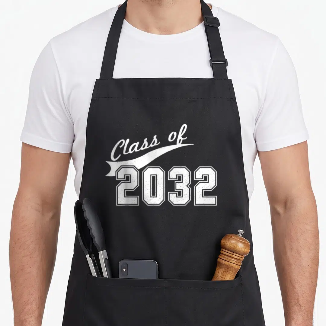 Kindergarten class funny apron - White Class of 2032 text on ribbon banner with block numerals — shown on a black cotton canvas apron against a white background