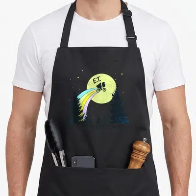 Extra rainbow apron - E.T. bicycle silhouette flying past yellow moon with rainbow trail between pine trees — shown on a black cotton canvas apron against a white background
