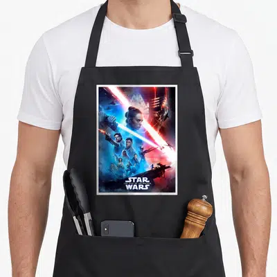 Rise character aprons - Rey and Kylo Ren poster with blue and red lightsaber clash and title text — shown on a black cotton canvas apron against a white background