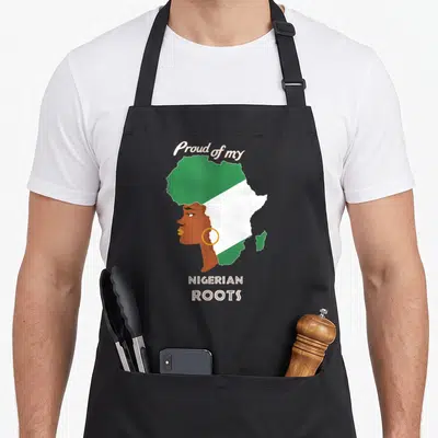 Proud nigerian apron - Woman profile merged with Nigeria flag map and Proud of my NIGERIAN ROOTS text — shown on a black cotton canvas apron against a white background
