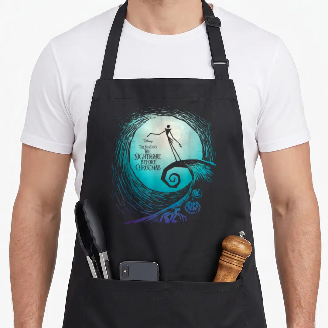 Movie jack apron - Jack Skellington silhouette on spiral hill with title text and pumpkins in blue purple swirl — shown on a black cotton canvas apron against a white background
