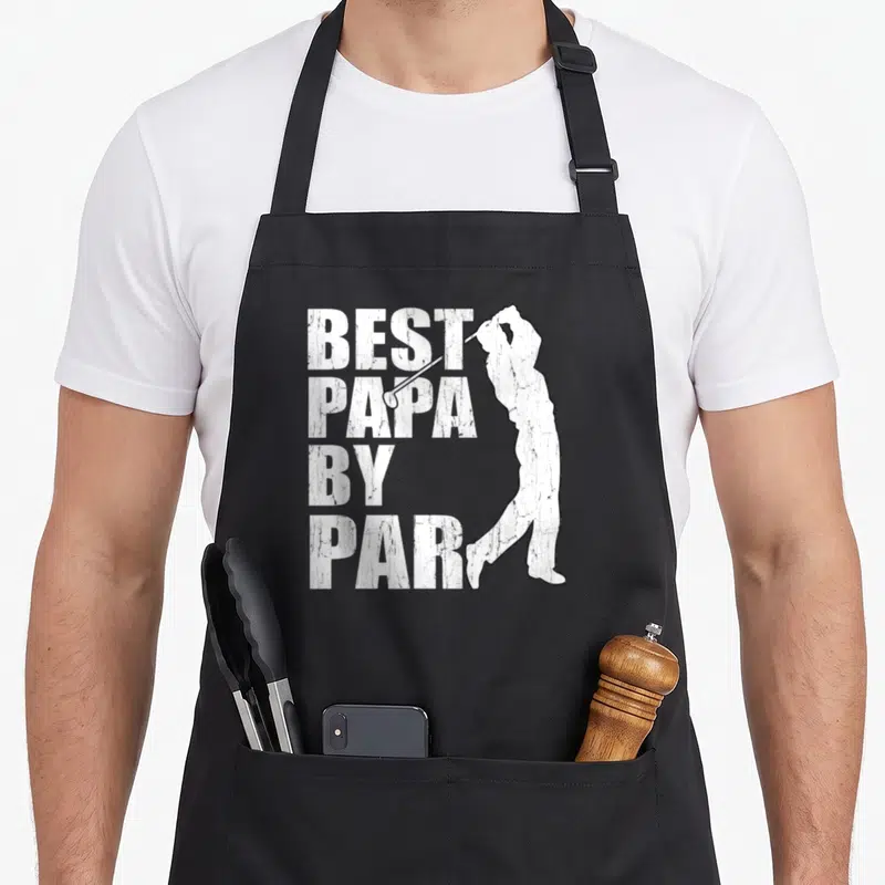 Papa golf apron - White distressed text Best Papa By Par with golfer silhouette on black apron — shown on a black cotton canvas apron against a white background
