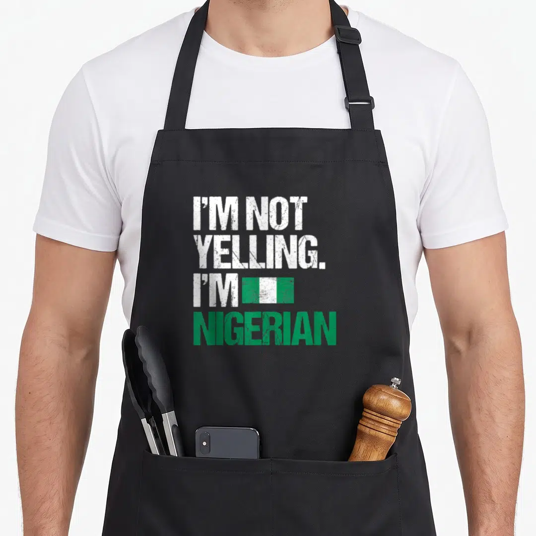 Yelling i love nigerian apron - I'M NOT YELLING I'M NIGERIAN text with green white flag graphic in distressed style — shown on a black cotton canvas apron against a white background