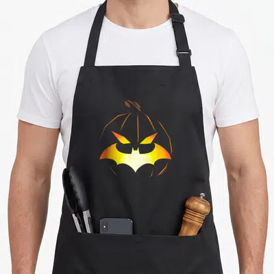 Jack bat halloween apron - Orange pumpkin outline with yellow orange bat symbol forming face features — shown on a black cotton canvas apron against a white background