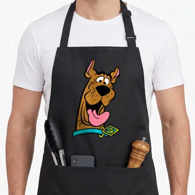 Costume october apron - Cartoon brown dog head with blue collar and yellow diamond tag — shown on a black cotton canvas apron against a white background