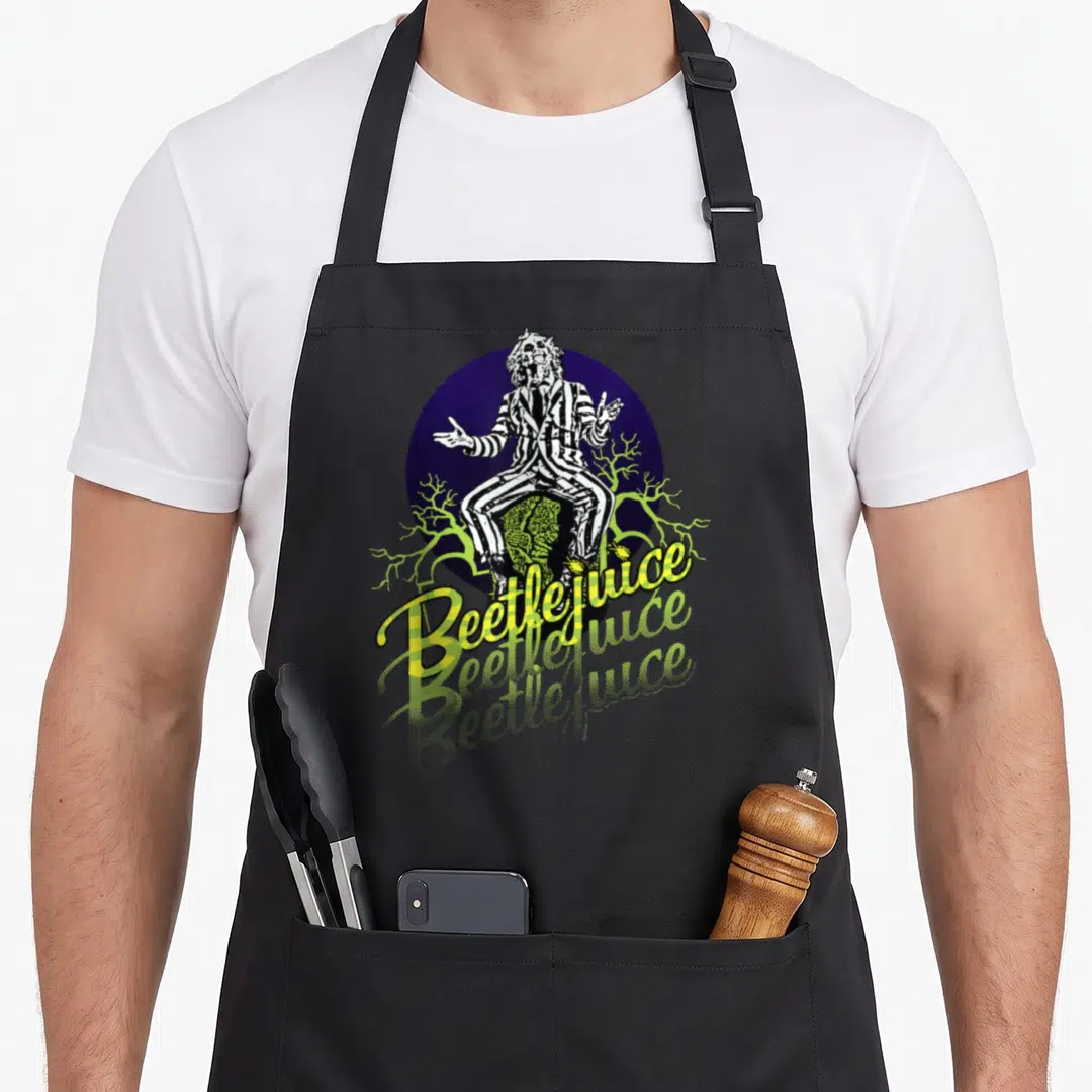 Three portrait novelty apron - Beetlejuice sitting on tombstone with purple circle and lime green branches and yellow — shown on a black cotton canvas apron against a white background