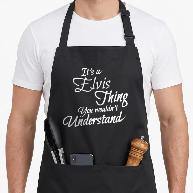 Elvis novelty apron - White stacked cursive text reading It's a Elvis Thing You wouldn't Understand — shown on a black cotton canvas apron against a white background