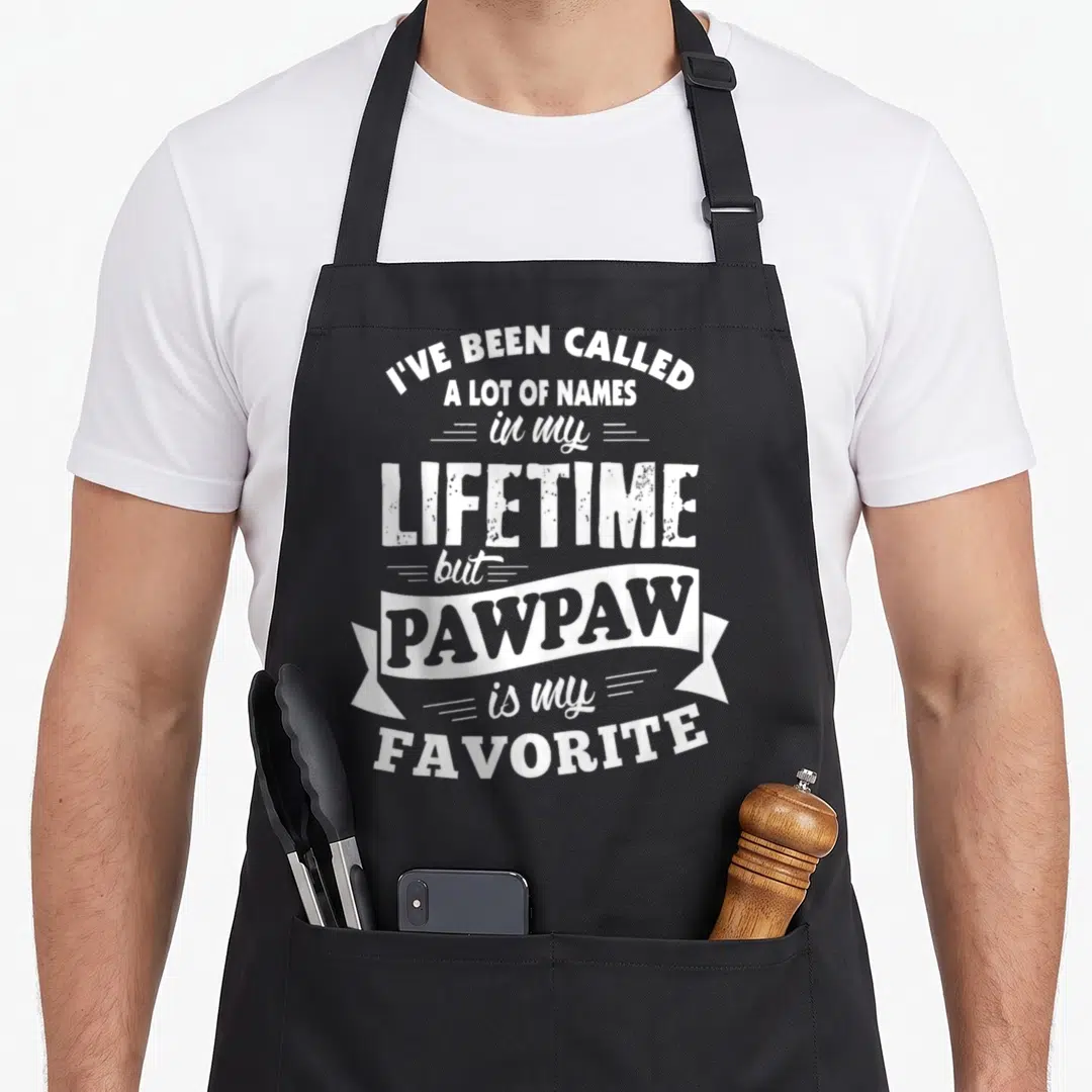Called lot of aprons - White typography reading I've Been Called a Lot of Names with PAWPAW inside a ribbon banner — shown on a black cotton canvas apron against a white background