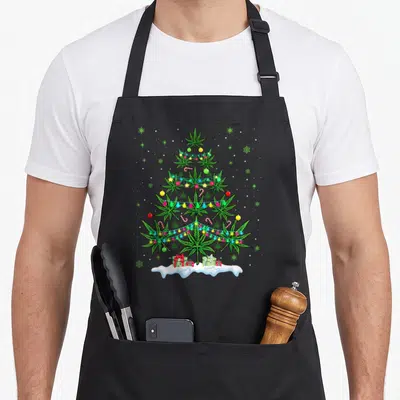 Cannabis smoking apron - Cartoon cannabis tree made of green leaves with red and yellow ornaments, candy canes — shown on a black cotton canvas apron against a white background