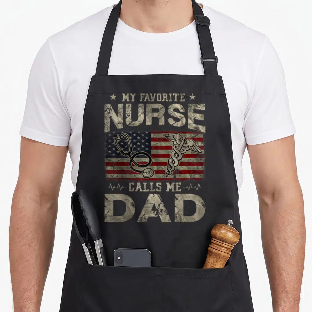 Flag nurses apron - Distressed beige text reading My Favorite Nurse Calls Me Dad over a USA flag with a stethoscope — shown on a black cotton canvas apron against a white background