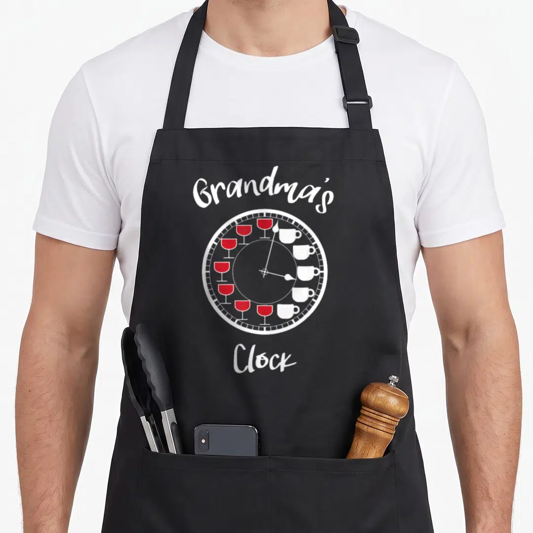 Coffee wine apron - White clock with red wine glasses and white coffee cups as numbers under Grandma's Clock text — shown on a black cotton canvas apron against a white background