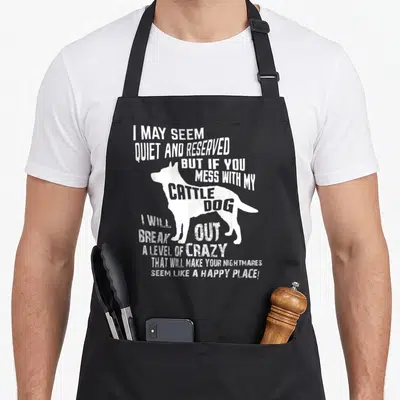 Cattle blue dog apron - White distressed cattle dog silhouette with sarcastic warning text stacked vertically — shown on a black cotton canvas apron against a white background