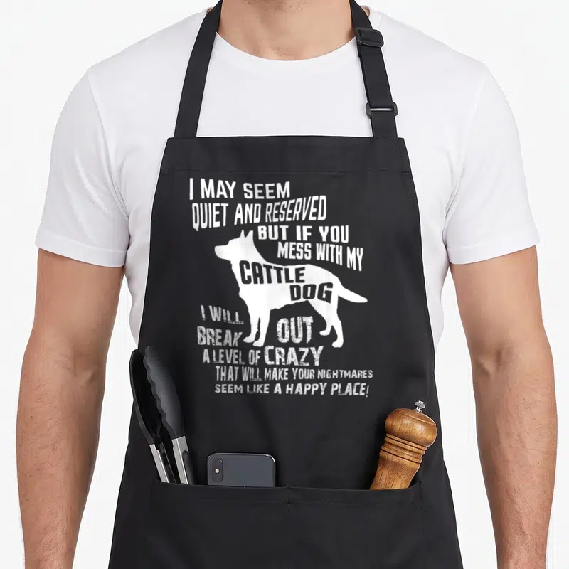 Cattle blue dog apron - White distressed cattle dog silhouette with sarcastic warning text stacked vertically — shown on a black cotton canvas apron against a white background