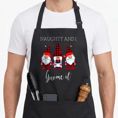Naughty buffalo apron - Three gnomes in red plaid with NAUGHTY AND I Gnome it text — shown on a black cotton canvas apron against a white background