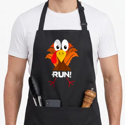Costume turkey apron - Cartoon turkey head chest with white RUN! text and red feet — shown on a black cotton canvas apron against a white background