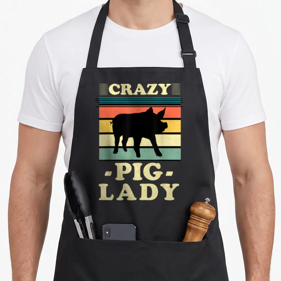 Cute crazy pig lady apron - Retro pig silhouette over red orange and green stripes with beige text — shown on a black cotton canvas apron against a white background