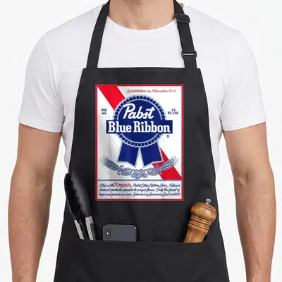 Label ribbon apron - Pabst Blue Ribbon beer label print with red stripe, blue seal, wheat, and hops on white background — shown on a black cotton canvas apron against a white background