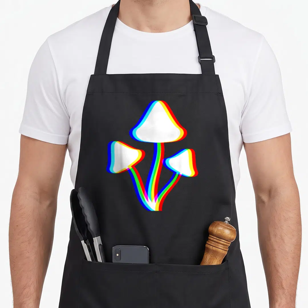 Trippy mushroom apron - Three cartoon mushrooms with white caps and layered white blue red outlines merging at stem base — shown on a black cotton canvas apron against a white background
