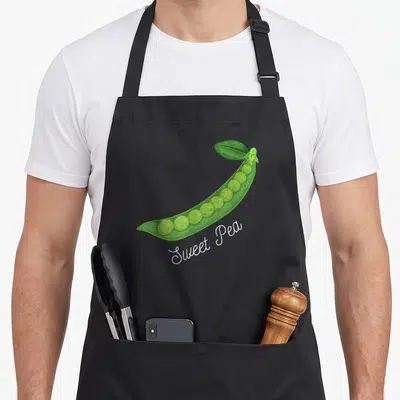 Pea vegetable apron - Green cartoon pea pod with white script text reading Sweet Pea — shown on a black cotton canvas apron against a white background