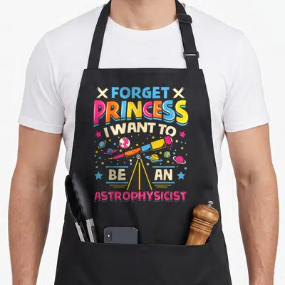 Funny forget princess apron - Cartoon telescope surrounded by planets and stars with multi-colored text — shown on a black cotton canvas apron against a white background