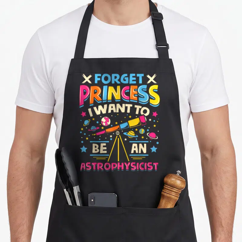 Funny forget princess apron - Cartoon telescope surrounded by planets and stars with multi-colored text — shown on a black cotton canvas apron against a white background
