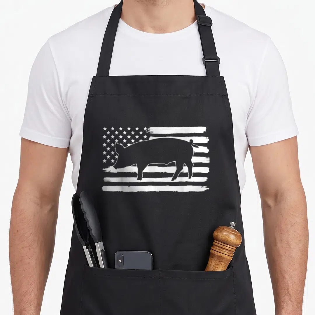 Pig 4th of july apron - White pig silhouette centered on a distressed USA flag graphic — shown on a black cotton canvas apron against a white background