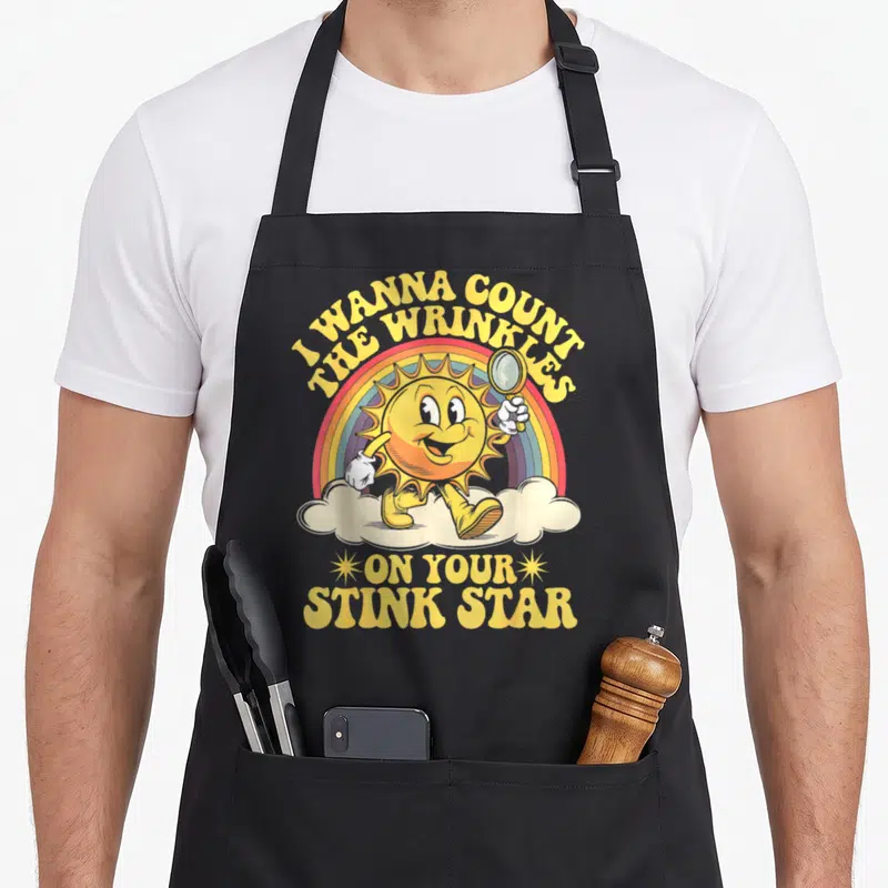 Count novelty apron - Cartoon sun holding magnifying glass on cloud with rainbow and yellow text — shown on a black cotton canvas apron against a white background