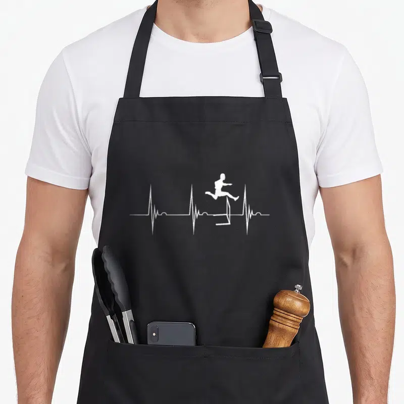 Hurdle track apron - White silhouette of person jumping over hurdle integrated into a horizontal heartbeat line — shown on a black cotton canvas apron against a white background