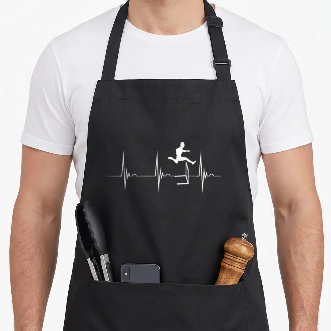 Hurdle track apron - White silhouette of person jumping over hurdle integrated into a horizontal heartbeat line — shown on a black cotton canvas apron against a white background