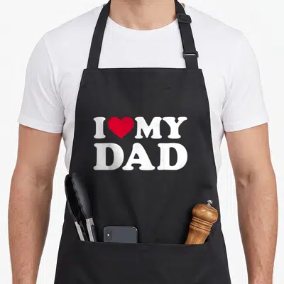Funny dad mode apron - White I MY DAD text with a red heart centered between the top words — shown on a black cotton canvas apron against a white background