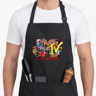 Mtv streetwear apron - Yellow TV logo over brick wall with cartoon spray cans and red MUSIC TELEVISION text — shown on a black cotton canvas apron against a white background