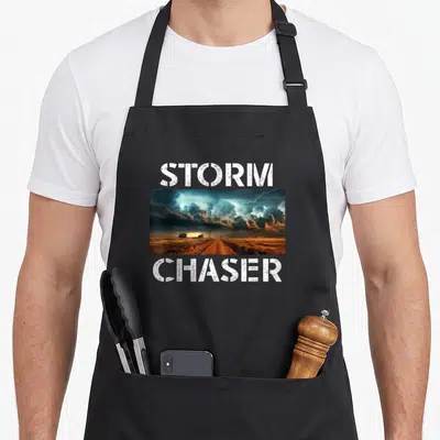 Extreme meteorologist apron - STORM CHASER text above and below a rectangular photo of a storm over a dirt road — shown on a black cotton canvas apron against a white background