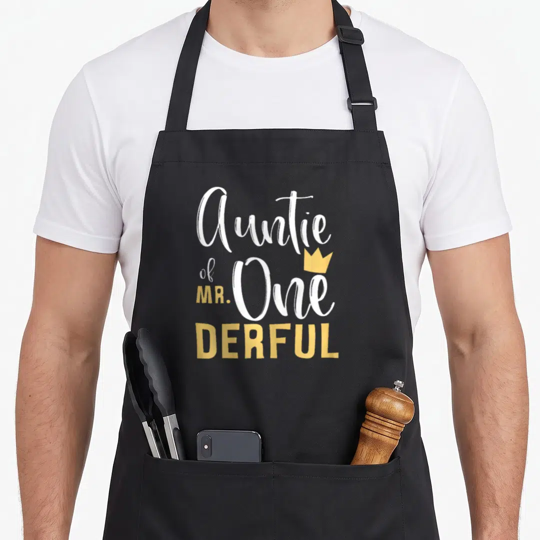 Derful birthday apron - Stacked text Auntie of MR One DERFUL with small yellow crown graphic — shown on a black cotton canvas apron against a white background
