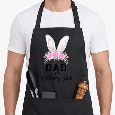Birthday family bunny apron - DAD of the Birthday Girl text under white bunny ears and pink roses — shown on a black cotton canvas apron against a white background