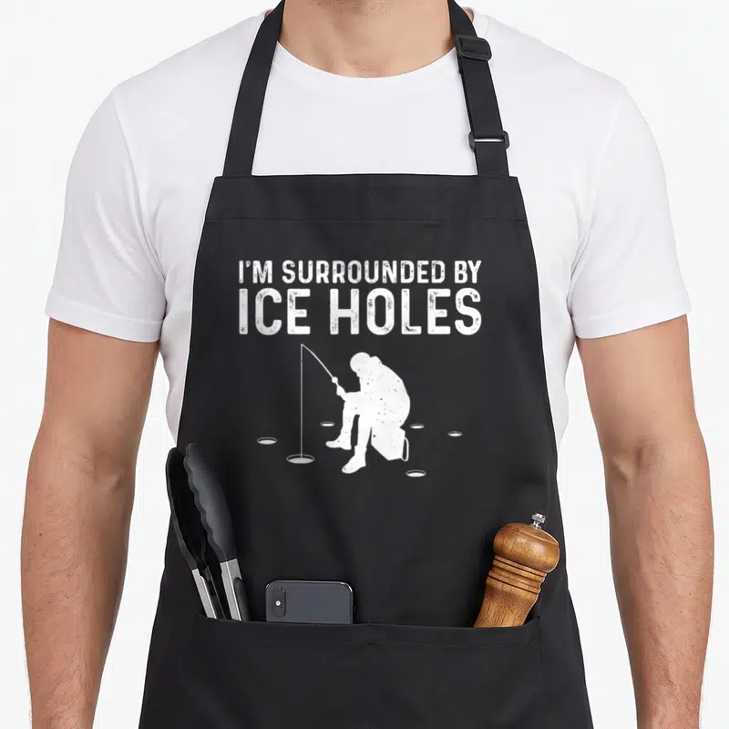 Snow fishing aprons - White fisherman silhouette surrounded by ice holes under stacked text — shown on a black cotton canvas apron against a white background