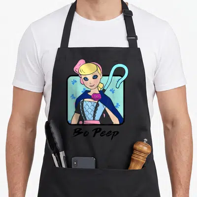 Peep colorful apron - Cartoon Bo Peep portrait with crook in black frame on light blue floral background — shown on a black cotton canvas apron against a white background