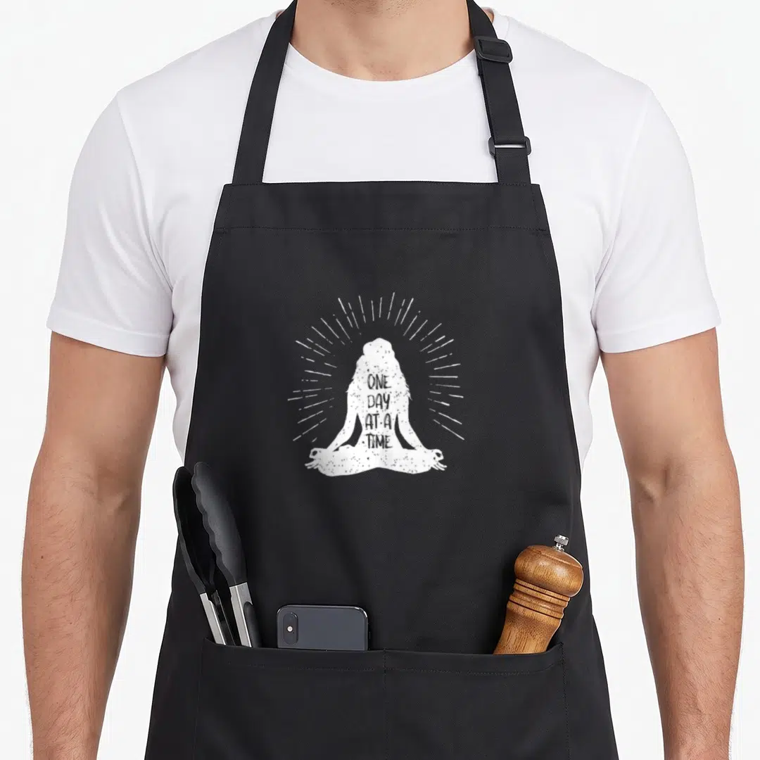 Odaat addiction recovery apron - White distressed silhouette of a person meditating with rays of light and stacked text — shown on a black cotton canvas apron against a white background