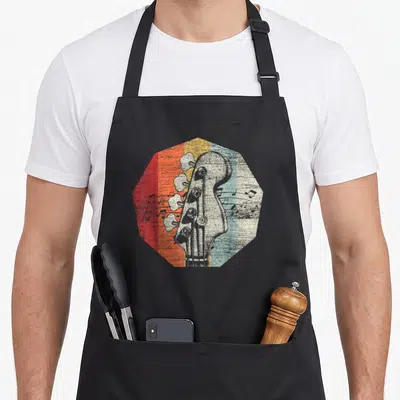 Bass guitarist apron - Retro bass headstock centered on red orange yellow blue grey white striped octagon — shown on a black cotton canvas apron against a white background
