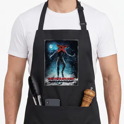 Demogorgon mountain apron - Realistic Demogorgon creature in snowy mountains with red head and DEMOGORGON text — shown on a black cotton canvas apron against a white background