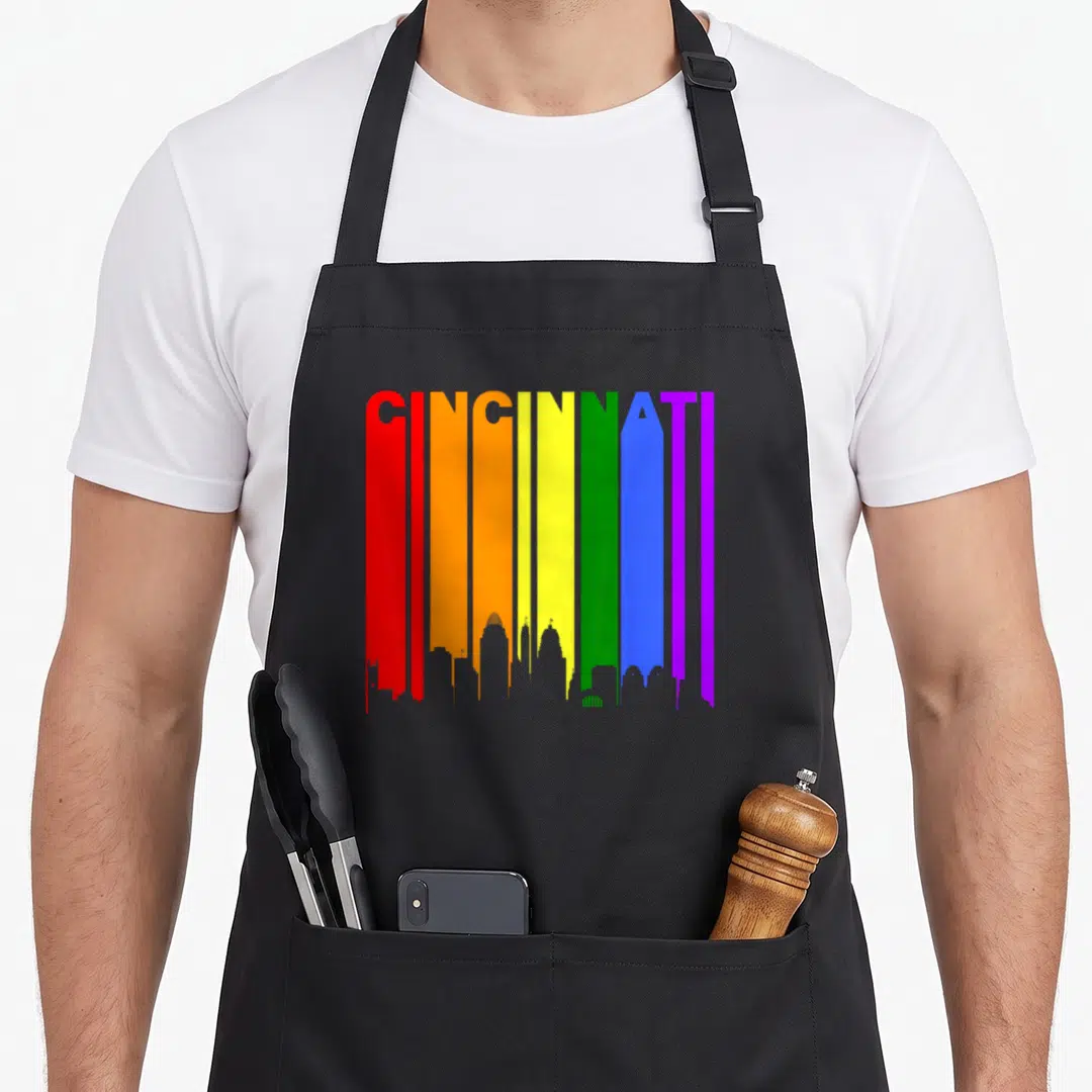Cincinnati gay pride apron - Rainbow CINGINNATI text forming skyline silhouette in red orange yellow green blue purple — shown on a black cotton canvas apron against a white background