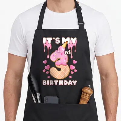 Birthday ice cream apron - Number 3 waffle cone with pink frosting, hearts, and IT'S MY rd BIRTHDAY text — shown on a black cotton canvas apron against a white background