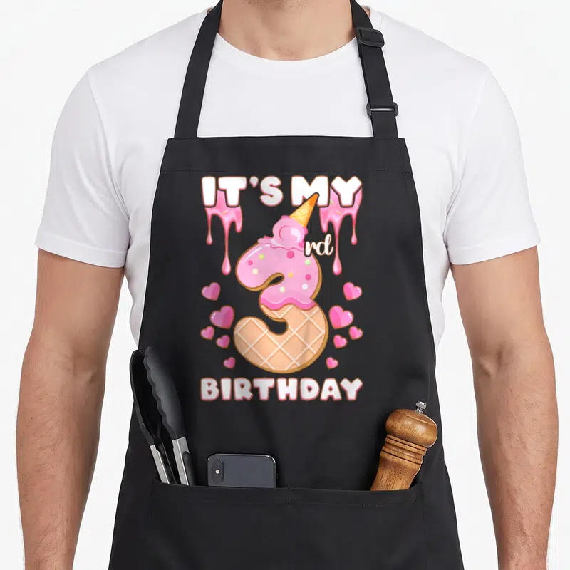 Birthday ice cream apron - Number 3 waffle cone with pink frosting, hearts, and IT'S MY rd BIRTHDAY text — shown on a black cotton canvas apron against a white background