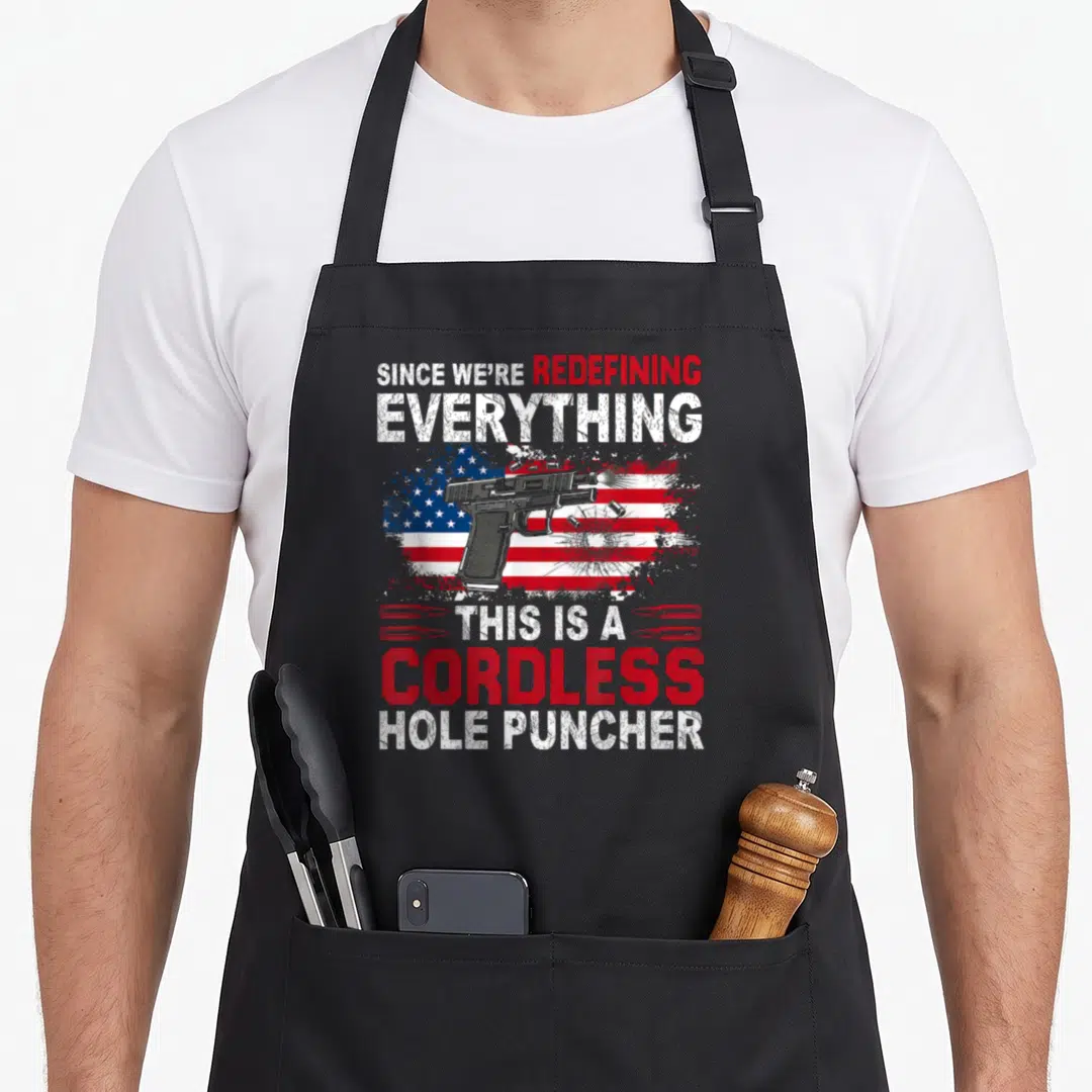 Cordless hole apron - Handgun over distressed US flag with text Since We Are Redefining Everything — shown on a black cotton canvas apron against a white background