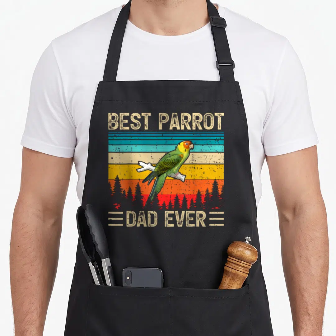 Parrot father day apron - Retro parrot on branch with best parrot dad ever text over colored stripes and red trees — shown on a black cotton canvas apron against a white background
