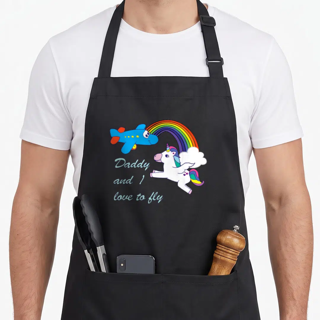 Unicorn chef and co aprons - Cartoon blue plane and white unicorn flying over rainbow with text Daddy and I love to fly — shown on a black cotton canvas apron against a white background