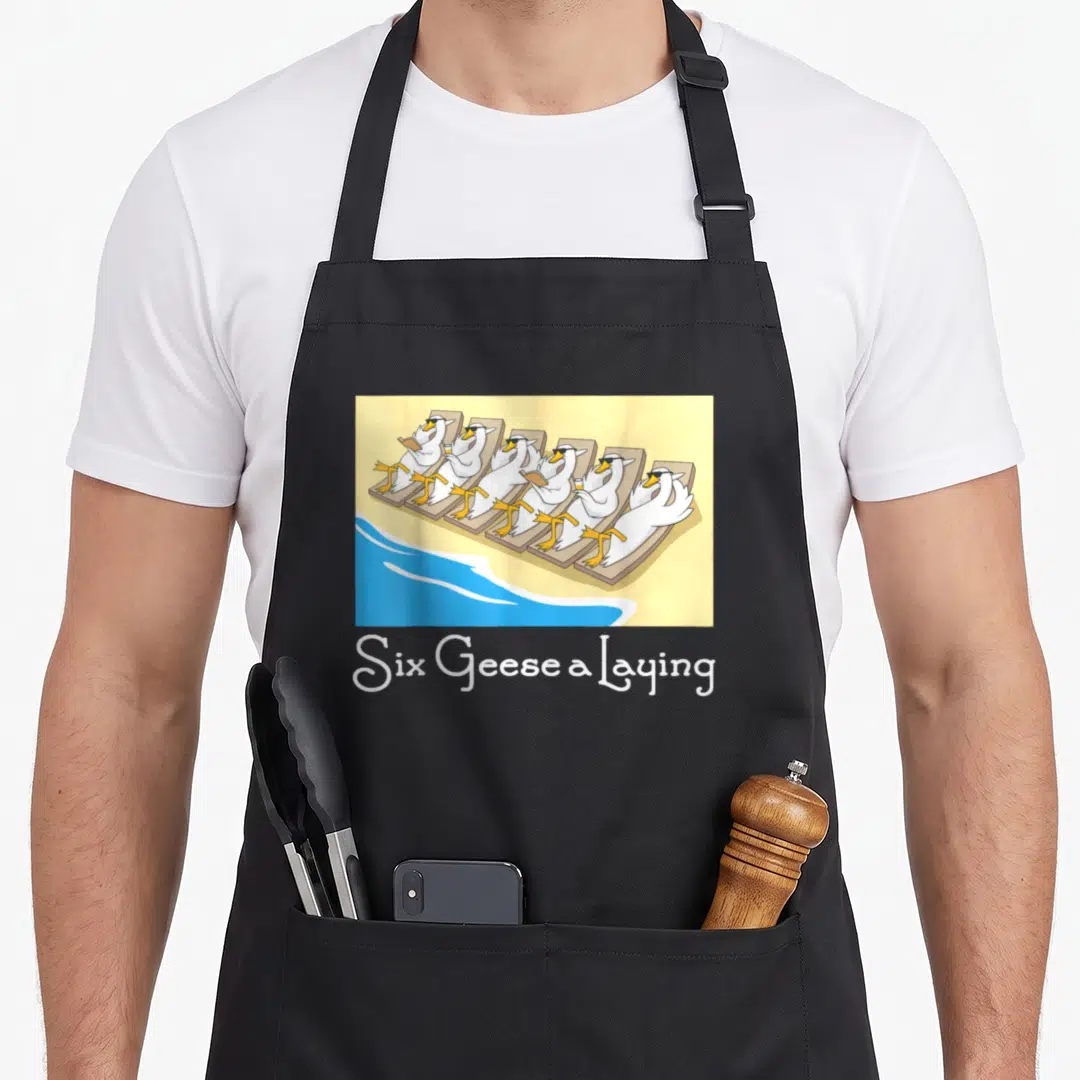 Geese christmas apron - Six Geese a Laying text below cartoon geese in sunglasses on beach chairs — shown on a black cotton canvas apron against a white background