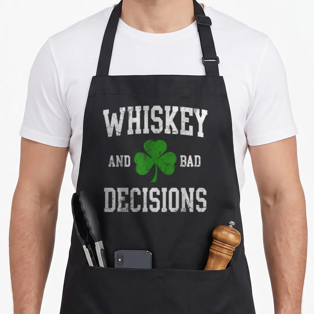 Decision funny irish aprons - Whiskey And Bad Decisions text surrounding a green shamrock in distressed style — shown on a black cotton canvas apron against a white background