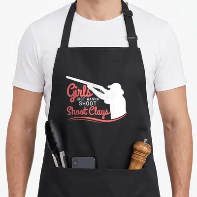 Shoot clay apron - White woman silhouette holding shotgun next to stacked coral and white text reading Girls Just Wanna — shown on a black cotton canvas apron against a white background